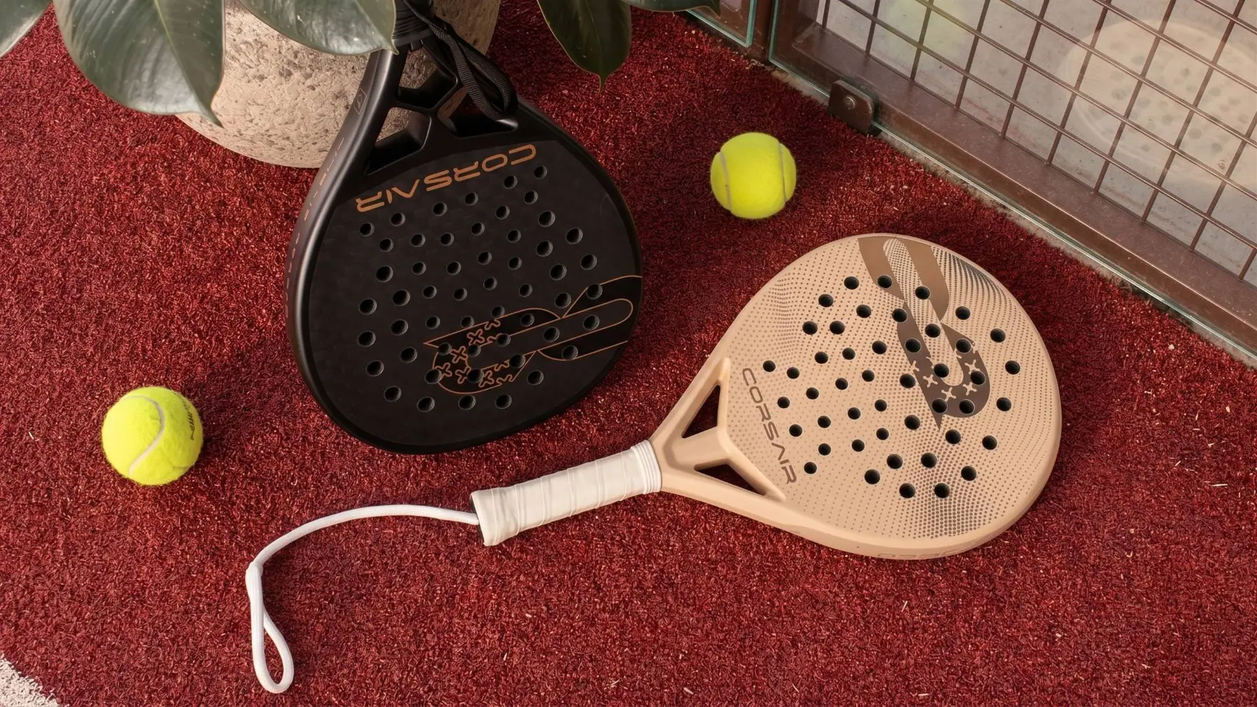 APEX and DROP at rest on a red court beside two balls, a plant and the glass at the edge of the court