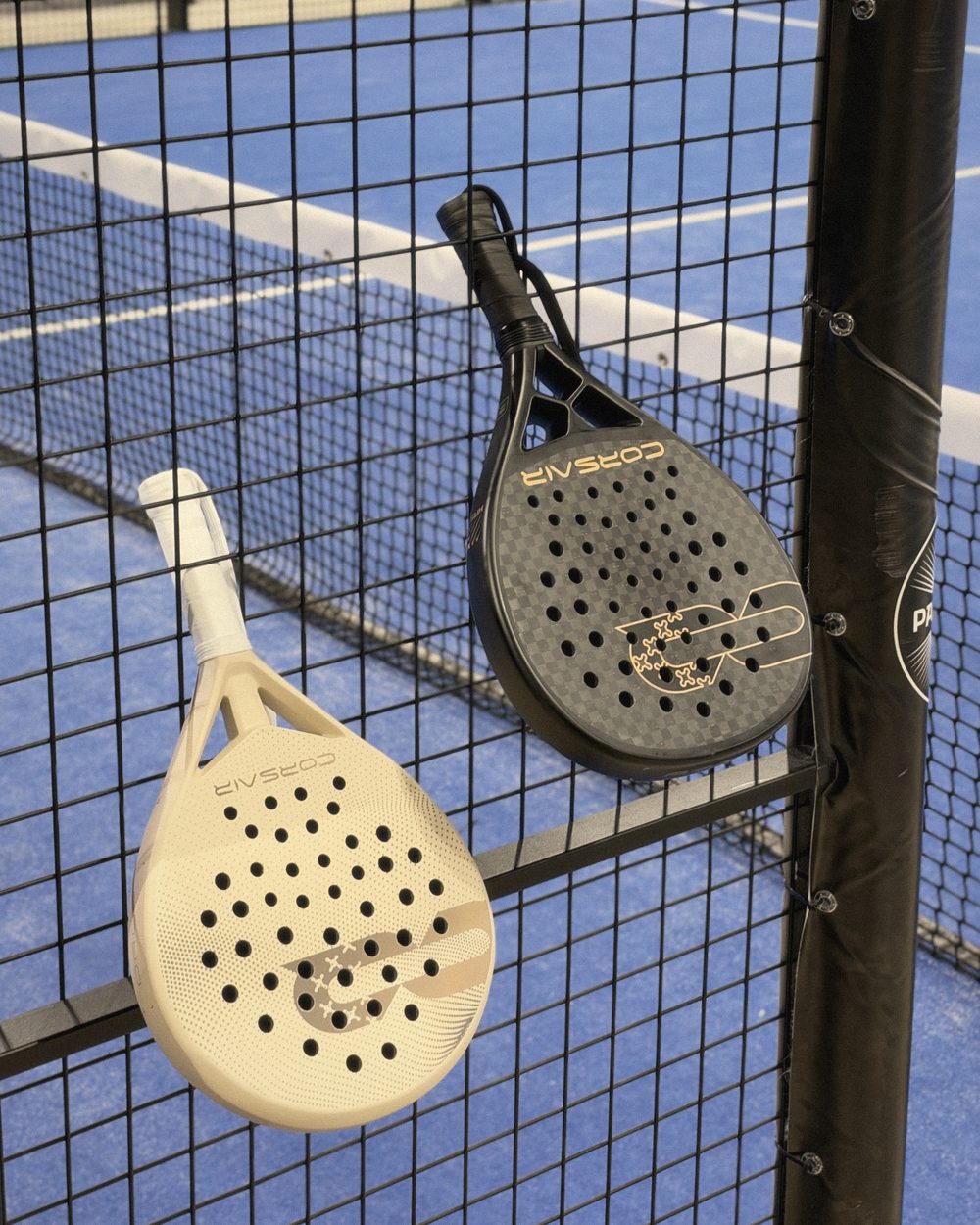 DROP and APEX hung on the mesh of an indoor court, blue courts beyond